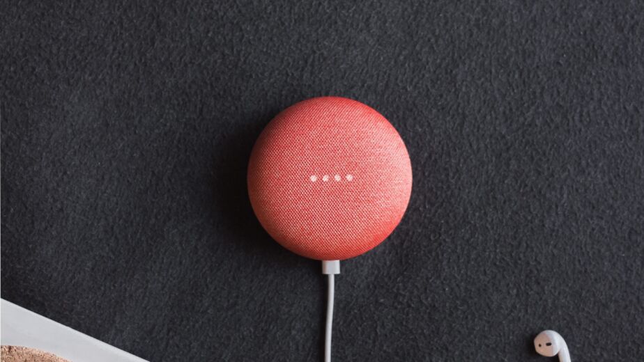 flat lay photography of coral Google Home Mini on black surface beside Apple AirPods
