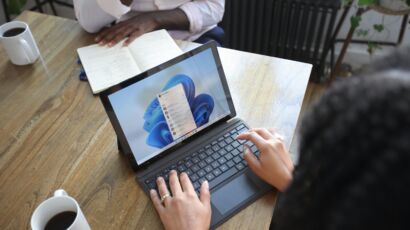 Overhead view of two people at a table working with a Microsoft laptop and notebook