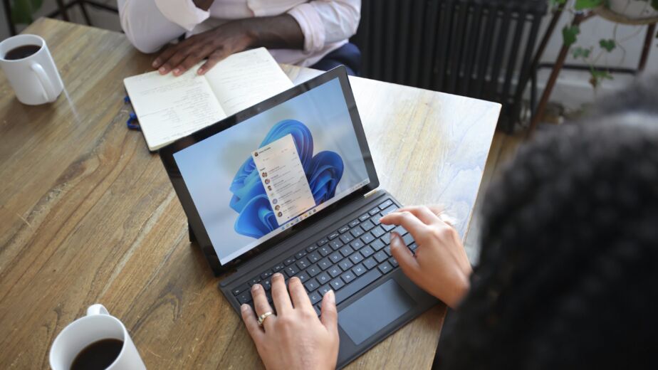 Overhead view of two people at a table working with a Microsoft laptop and notebook