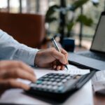 Free A person calculating finances with a calculator and pen on a desk indoors. Stock Photo