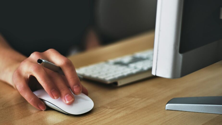 Free A hand using a wireless mouse at a modern desk setup with a computer and keyboard. Stock Photo
