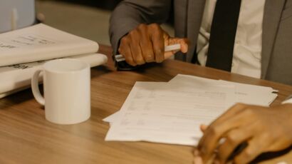 Free Close-up of a businessman holding and reviewing documents on a wooden desk. Stock Photo