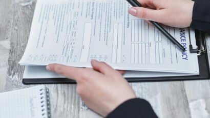 Free Close-up of hands analyzing insurance policy paperwork with pen on table. Stock Photo